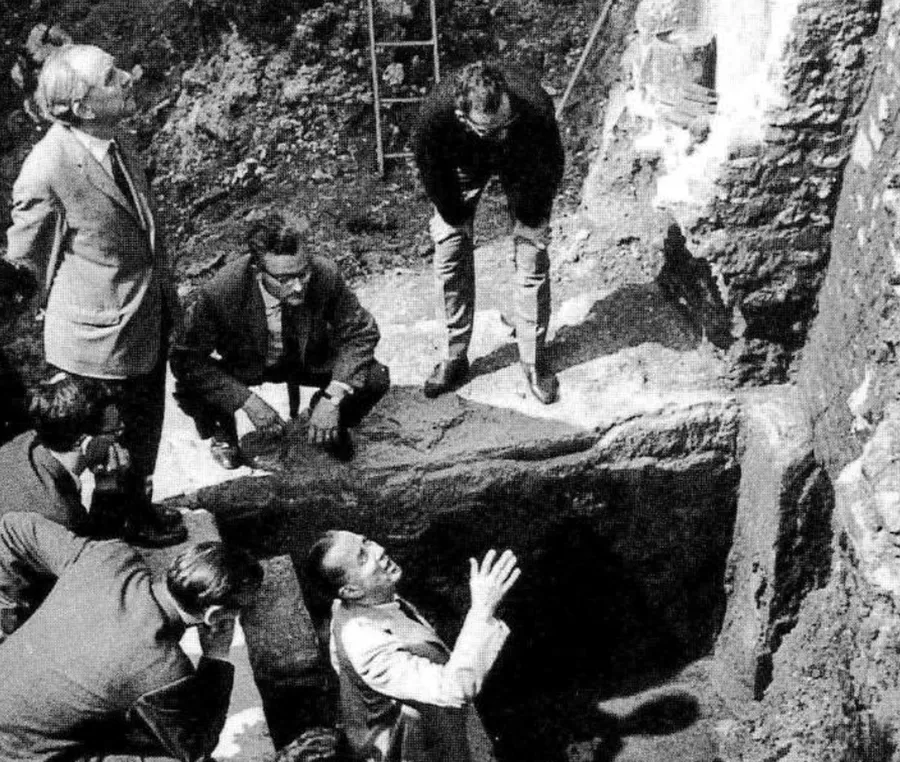 The excavation of the Roman bathhouse beneath Op de Thermen in Maastricht, in black and white: men in suits gather around a pit between old stone walls, one of them standing in it and looking up